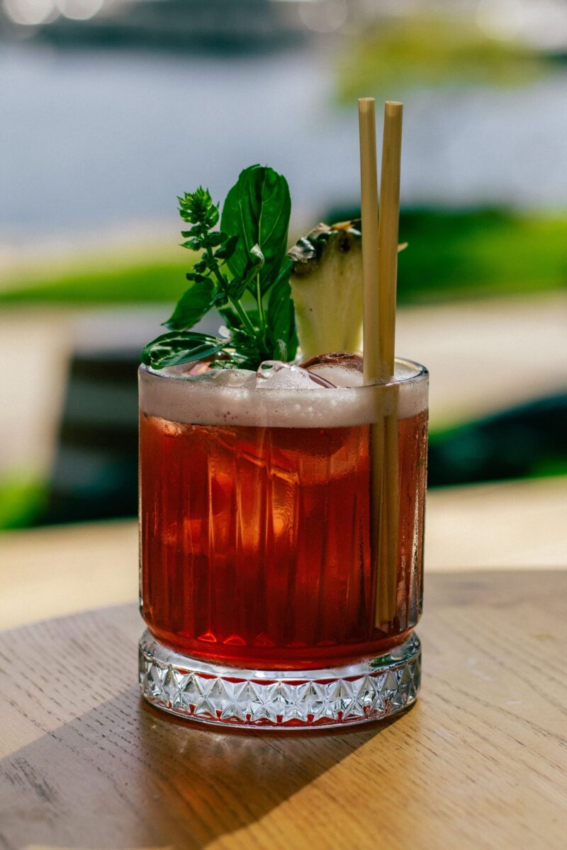 Iced cocktail with herbs and pineapple garnish, served outdoors on a sunny day.
